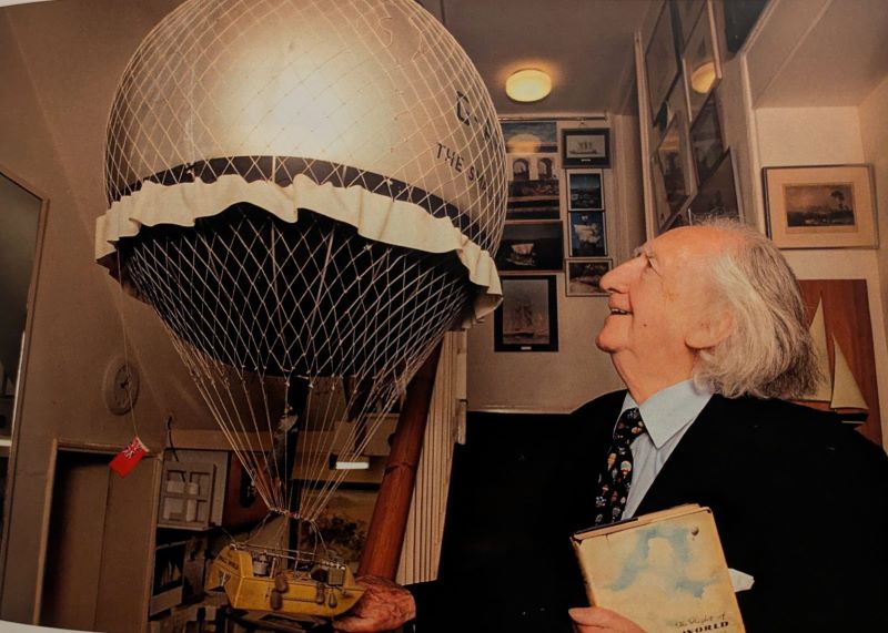 A picture of the model balloon hanging in Colin Mudie's home with a smiling Colin Mudie looking at it.